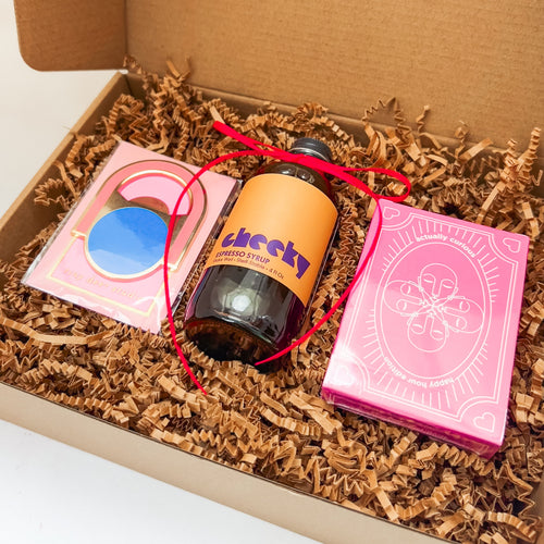 Gift box with a bottle of cocktail syrup, a card game, and a bottle opener on a light background